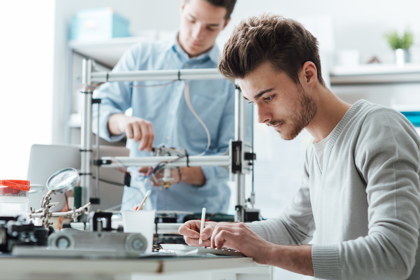 Engineering students working in the lab, a student is using a 3D printer in the background