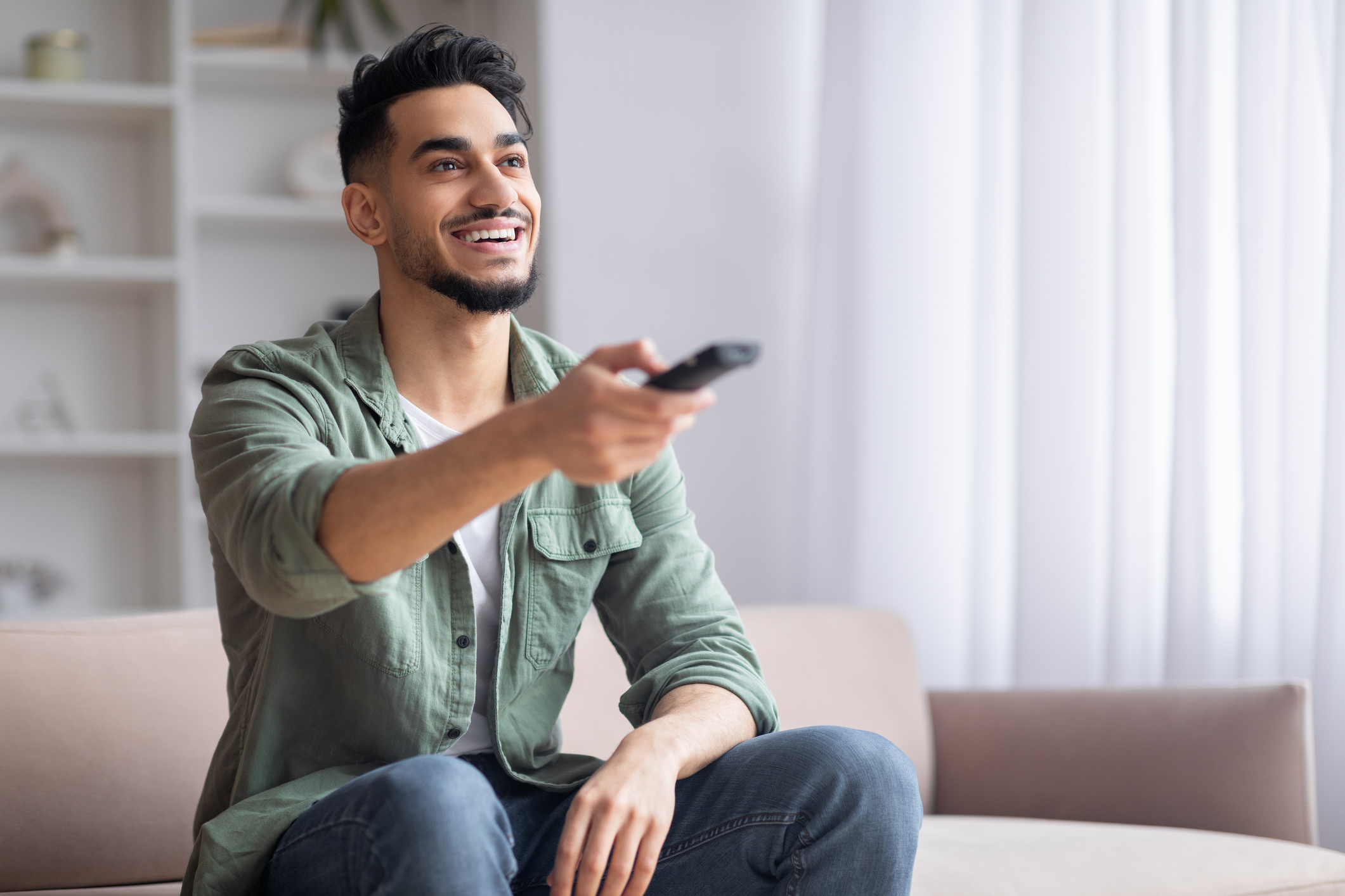 Smiling guy with beard sits on sofa ,