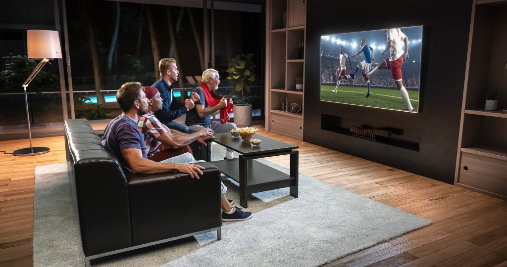 a group of people watching football on a large smart TV.